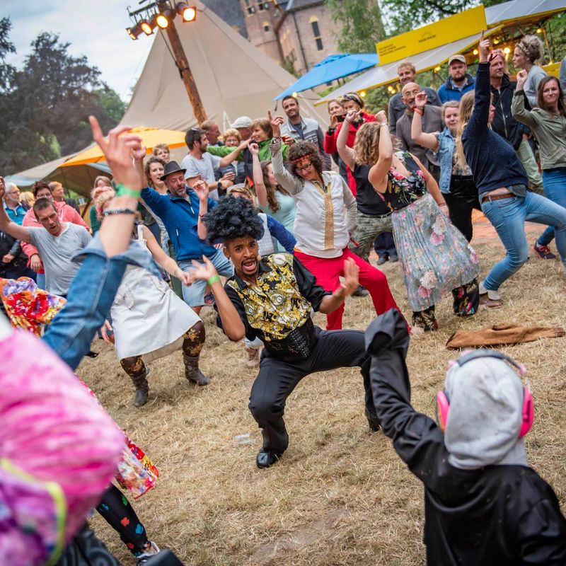 Performer in a gold vest dancing low, surrounded by a festival crowd